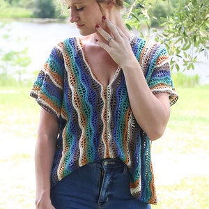 May include: A crocheted top with a striped pattern in shades of blue, green, brown, and white. The top has a V-neck and short sleeves.