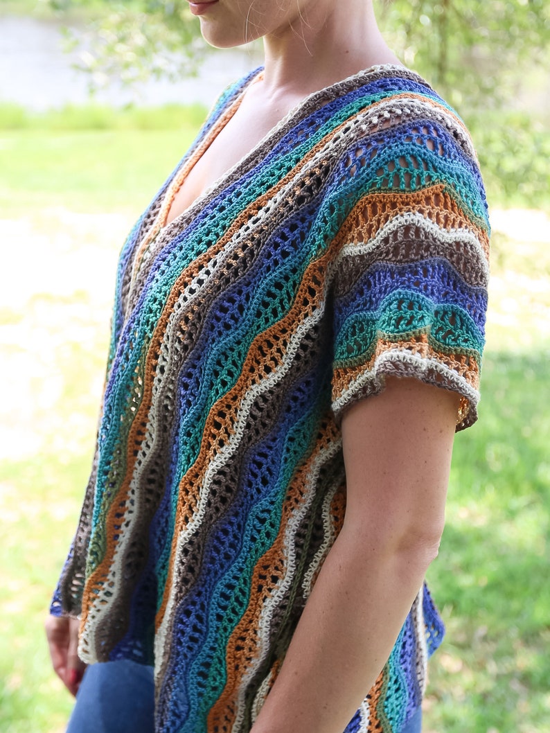 Pu&ograve; includere: Un top all'uncinetto con un motivo a righe ondulate in tonalit&agrave; di blu, verde, marrone e arancio. Il top ha una scollatura a V e maniche corte.
