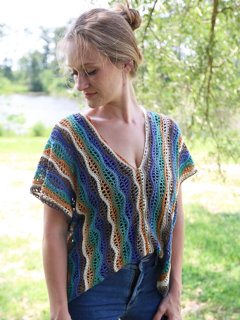 Pu&ograve; includere: Un top all'uncinetto con un motivo a righe in tonalit&agrave; di blu, verde, marrone e bianco. Il top ha una scollatura a V e maniche corte.