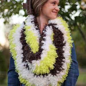May include: A white, brown, and lime green fuzzy scarf. The scarf is worn around the neck of a person wearing a denim jacket.
