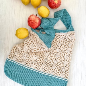 May include: A crocheted tote bag with a teal blue bottom and a beige top. The bag is made of a delicate, open-weave pattern. The bag is surrounded by lemons and apples.