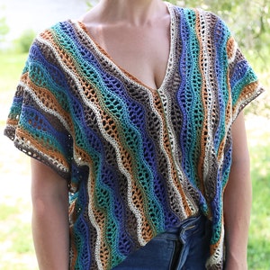 Pu&ograve; includere: Un top all'uncinetto con un motivo a righe in tonalit&agrave; di blu, verde, marrone e bianco. Il top ha una scollatura a V e maniche corte.