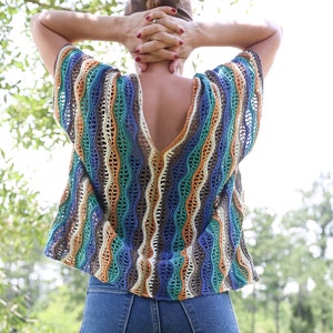 Pu&ograve; includere: Una donna indossa una maglia a uncinetto a righe blu, arancio e marrone con una scollatura a V profonda e una vestibilit&agrave; ampia. Indossa jeans blu.