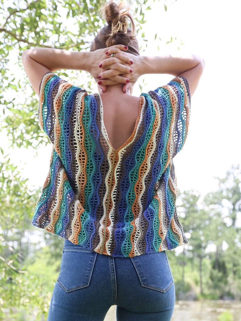 Pu&ograve; includere: Una donna indossa una maglia a uncinetto a righe blu, arancio e marrone con una scollatura a V profonda e una vestibilit&agrave; ampia. Indossa jeans blu.