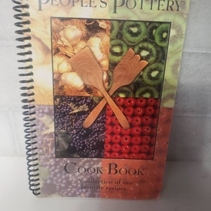 May include: A spiral bound cookbook with a colorful cover featuring a collage of fruits, vegetables, and wooden kitchen utensils. The title is "People's Pottery Cook Book" and the subtitle is "A collection of our favorite recipes."