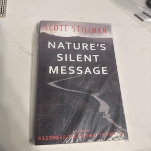 May include: A book titled "Nature's Silent Message" by Scott Stillman, wrapped in clear plastic. The cover features a dark landscape with a winding road and the author's name in red.