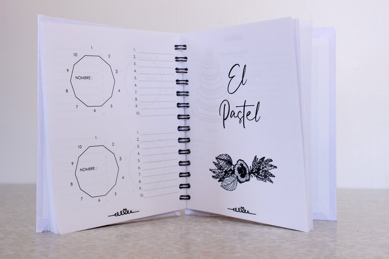 May include: An open notebook with white pages and a black spiral binding. The left page features two geometric diagrams with numbered sides and the word "NOMBRE:" The right page has the words "El Pastel" in cursive and a floral illustration.