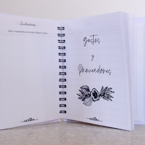 May include: Open white spiral-bound notebook with lined pages. The left page has the word "Invitaciones" and the right page has "gastos y Proveedores" in script. A floral illustration is below the text. The notebook is open on a light surface.