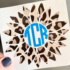 May include: A vinyl decal featuring a sunflower with a leopard print pattern and a blue circle with the monogram "TCR" in the center.