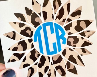 May include: A vinyl decal featuring a sunflower with a leopard print pattern and a blue circle with the monogram "TCR" in the center.