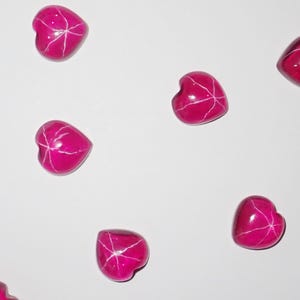 May include: Six pink heart-shaped stones with white veins, scattered on a white background.