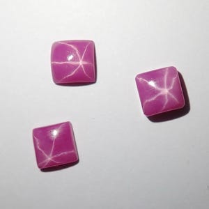 May include: Three pink star ruby cabochons, each with a six-pointed star in the center.