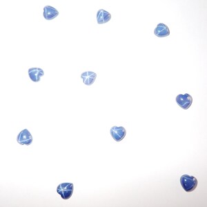 Puede incluir: Un conjunto de gemas azules en forma de corazón con un patrón de estrella. Las gemas están dispersas sobre un fondo blanco, mostrando su forma y color únicos. Estas gemas podrían usarse para hacer joyas o como elementos decorativos.