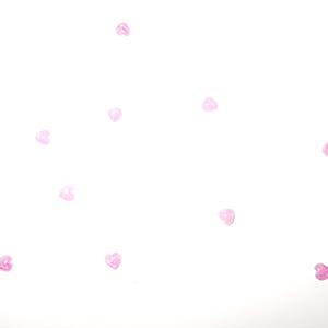 May include: A collection of small, translucent, pale pink heart-shaped beads on a white backdrop. The beads are scattered, creating a delicate and romantic aesthetic. Suitable for crafting or embellishments.