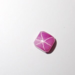 May include: A pink star ruby gemstone with a square shape.