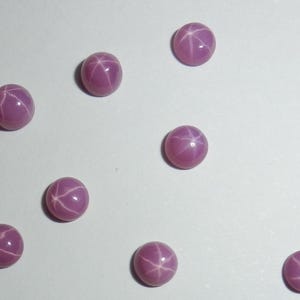 May include: Nine pink star sapphires with a starburst pattern. The sapphires are round and have a smooth, polished finish.