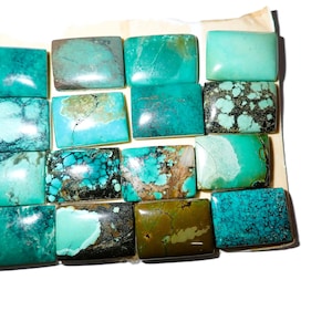 Op de afbeelding: Een verzameling van vijftien rechthoekige turkoois cabochons gerangschikt in een raster. De stenen vertonen verschillende tinten blauw en groen, met natuurlijke matrixpatronen, donkere aders en gladde, gepolijste oppervlakken met een glans.