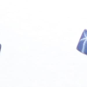 May include: Two small, square-shaped, blue star sapphires with a white star pattern.
