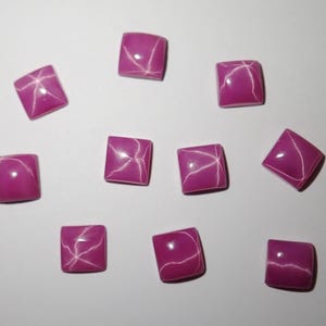 Peut inclure: Dix pierres précieuses de rubis étoilés roses avec un motif en étoile. Les pierres précieuses sont de forme carrée et ont une finition polie.