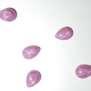 Op de afbeelding: Vijf roze ster-saffieren in peer-vorm. De saffieren zijn gefacetteerd en hebben een wit ster-patroon.