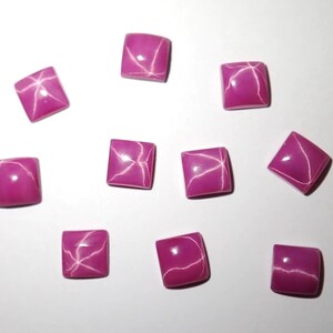 Peut inclure: Un ensemble de neuf petits cabochons de forme carrée d'une couleur rose magenta vive. Chaque pièce présente une surface lisse et polie avec une finition brillante qui reflète la lumière, créant un motif en forme d'étoile sur le dessus.