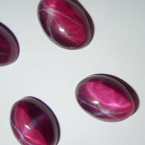 May include: Four oval-shaped, pink star ruby cabochons with a white star effect.