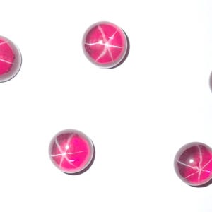 May include: Six round, pink star ruby cabochons on a white background.