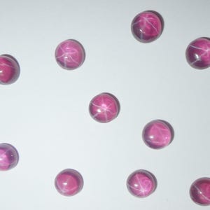 May include: Ten round, pink star ruby cabochons with a white star pattern.
