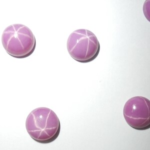 May include: Five pink star sapphires with a white star pattern. The sapphires are round and cabochon cut.