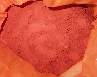 Puede incluir: Primer plano de un polvo rojo vibrante, que llena el encuadre. El polvo tiene una apariencia fina y texturizada, lo que sugiere que está finamente molido. Está contenido dentro de una bolsa naranja translúcida, creando un contraste de color y textura.