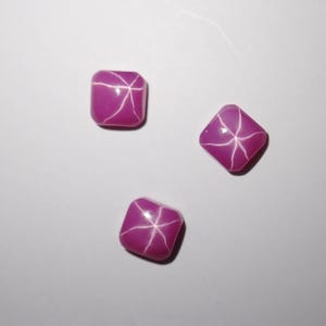 May include: Three pink star ruby cabochons, each with a six-pointed star in the center.