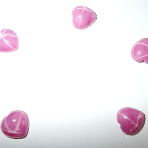 Puede incluir: Cinco gemas rosas en forma de corazón con patrones de estrella blancos. Las gemas están dispuestas en un patrón circular sobre un fondo blanco. Cada piedra tiene una superficie lisa y pulida, y los patrones de estrella irradian desde el centro.