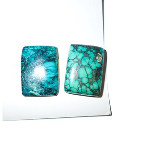 May include: Two rectangular turquoise gemstones with a mottled pattern of teal and dark green. The stones are polished and have a glossy finish, set against a white background. The gemstones are likely for jewelry making.