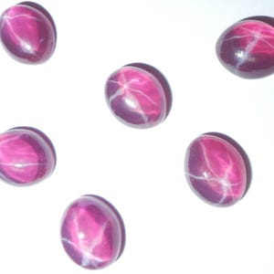 May include: Six oval-shaped pink star ruby gemstones with a white star in the center.