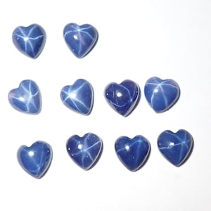 Puede incluir: Colección de diez gemas pulidas en forma de corazón. Cada gema es de color azul oscuro con un patrón en forma de estrella en su superficie. Las gemas están dispuestas sobre un fondo blanco.