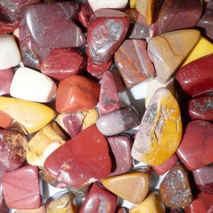 May include: A collection of polished tumbled stones in various shapes and sizes. The stones feature a vibrant colour palette including deep red, mustard yellow, cream, and brown, with smooth, glossy surfaces and natural mineral veining throughout.