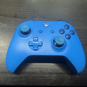 May include: A bright blue wireless video game controller featuring a central Xbox logo button, two analog sticks with light blue caps, a directional pad, and four action buttons labeled A, B, X, and Y, along with menu and view buttons.
