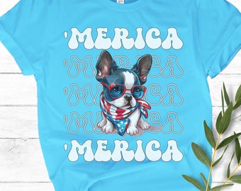 May include: Light blue t-shirt featuring a cartoon dog wearing red glasses and a patriotic bandana. The word "'MERICA" is printed in white, stacked multiple times. The dog has black and white fur.