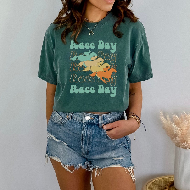May include: A green t-shirt with a retro design featuring the text "Race Day" repeated with a graphic of horses running.