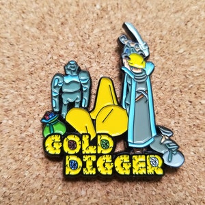 Puede incluir: Un pin de esmalte amarillo y azul con un personaje de dibujos animados que sostiene una espada y una bolsa de monedas de oro. El texto "GOLD DIGGER" está escrito en letras amarillas con contornos negros.