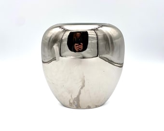 Può includere: Un vaso d'argento a forma di mela con una superficie liscia e riflettente.