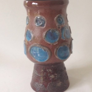Könnte beinhalten: Eine braune Keramikvase mit einem ausgestellten oberen Teil und einem Sockel. Die Vase ist mit blauen und braunen Kreisen verziert.