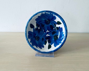 Könnte beinhalten: Eine weiße Keramikschüssel mit blauem Blumendesign. Die Schüssel zeigt ein stilisiertes Blumenmuster mit blauen Blüten und grünen Blättern.