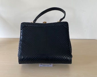 May include: A black snakeskin handbag with a gold clasp and a top handle.