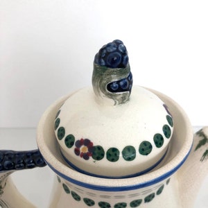 May include: White ceramic coffee pot with a blue and green floral design. The lid has a blue and green floral knob.