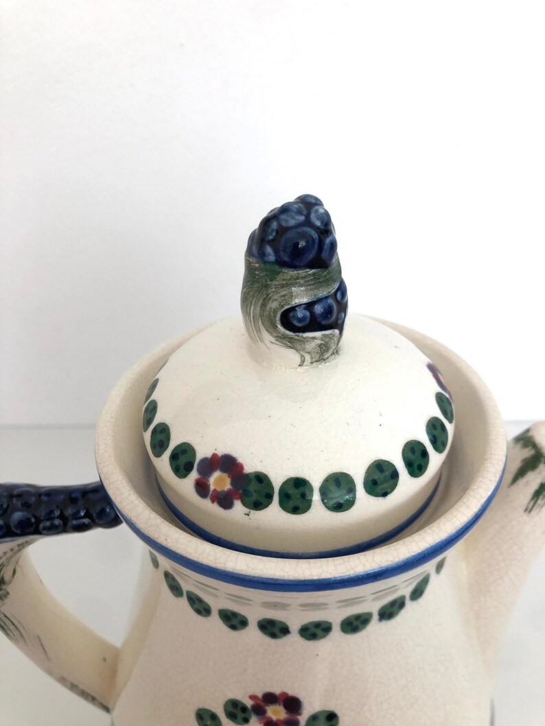 May include: White ceramic coffee pot with a blue and green floral design. The lid has a blue and green floral knob.