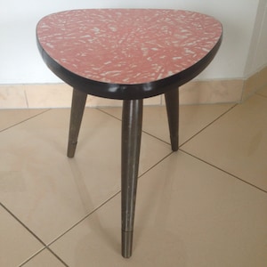 May include: A pink and white speckled three-legged table with a black rim and black wooden legs.