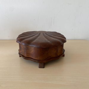 以下が含まれることがあります： 茶色の仕上げをした貝殻の形をした木製の箱。箱には蓋があり、4本の小さな足で立っています。