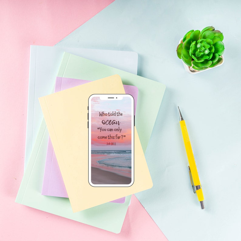 May include: A smartphone with a quote from the Bible, "Who told the ocean "You can only come this far?" Job 36:11", displayed on the screen. The phone is on top of a stack of colorful notebooks, with a yellow pencil and a small potted succulent plant on a light blue background.
