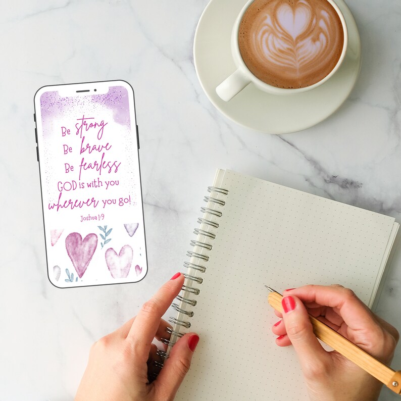 May include: A phone screen displaying a motivational quote with a watercolor background. The quote reads "Be strong, Be brave, Be fearless, GOD is with you wherever you go! Joshua 19". The background is a soft purple and pink with watercolor hearts and leaves.
